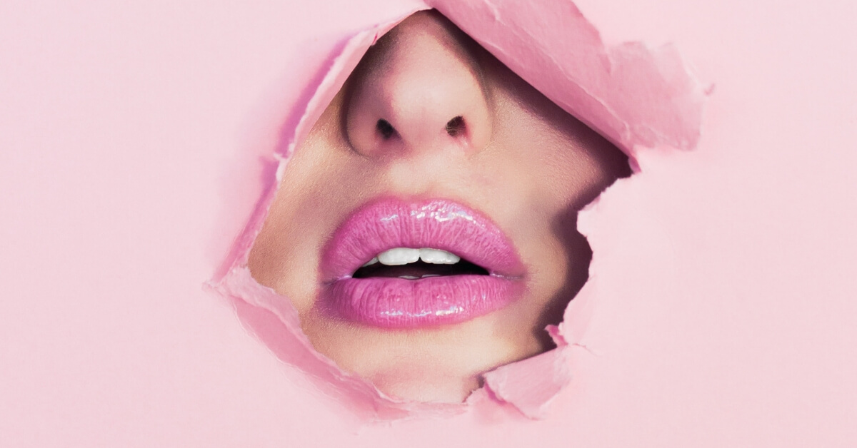 woman's lips with pink lipstick showing through hole in pink wallpaper