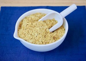 Nutritional yeast flakes in white bowl on blue cloth