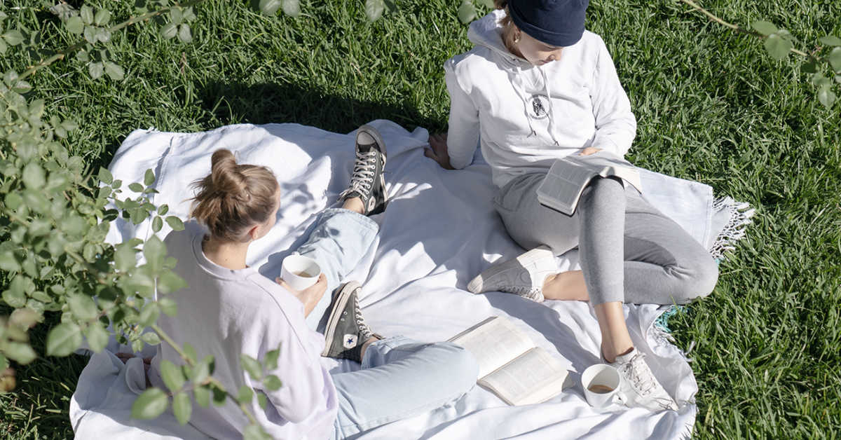 women reading their bibles on white picnic rug in sun