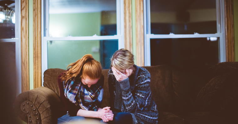 Two people sitting on couch looking down and sad