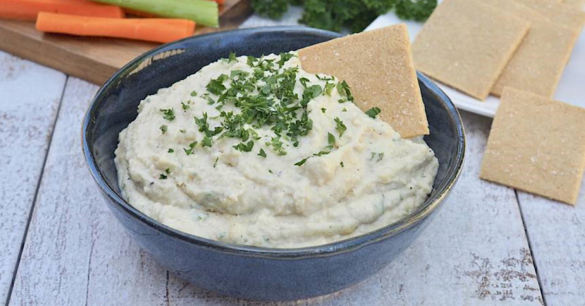 bowl of french onion dip sprinkled with herbs and a cracker dipped in
