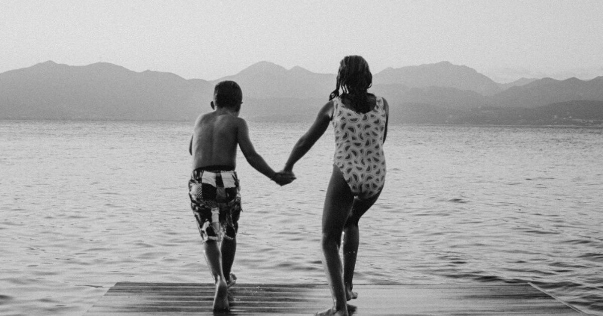 black and white photo of two kids in bathing suits holding hands jumping off a pier into the water