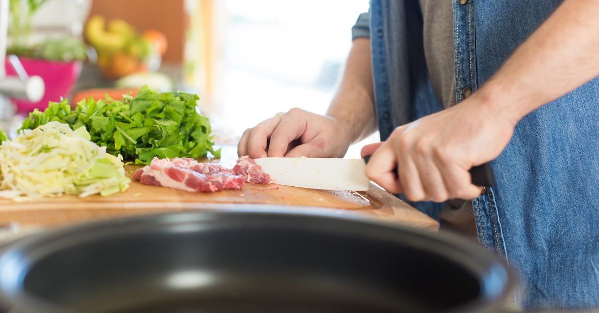 person chopping veges and meat in a kitchen