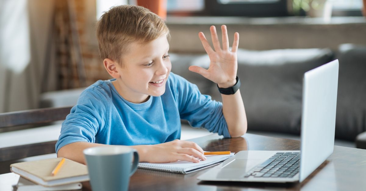 photo of a boy waving at the screen of his computer. schools may have more flexible learning options after covid-19