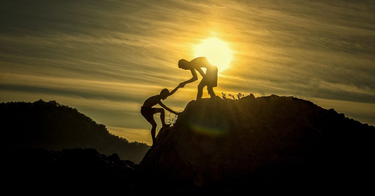 photo of a man helping another man up a mountain