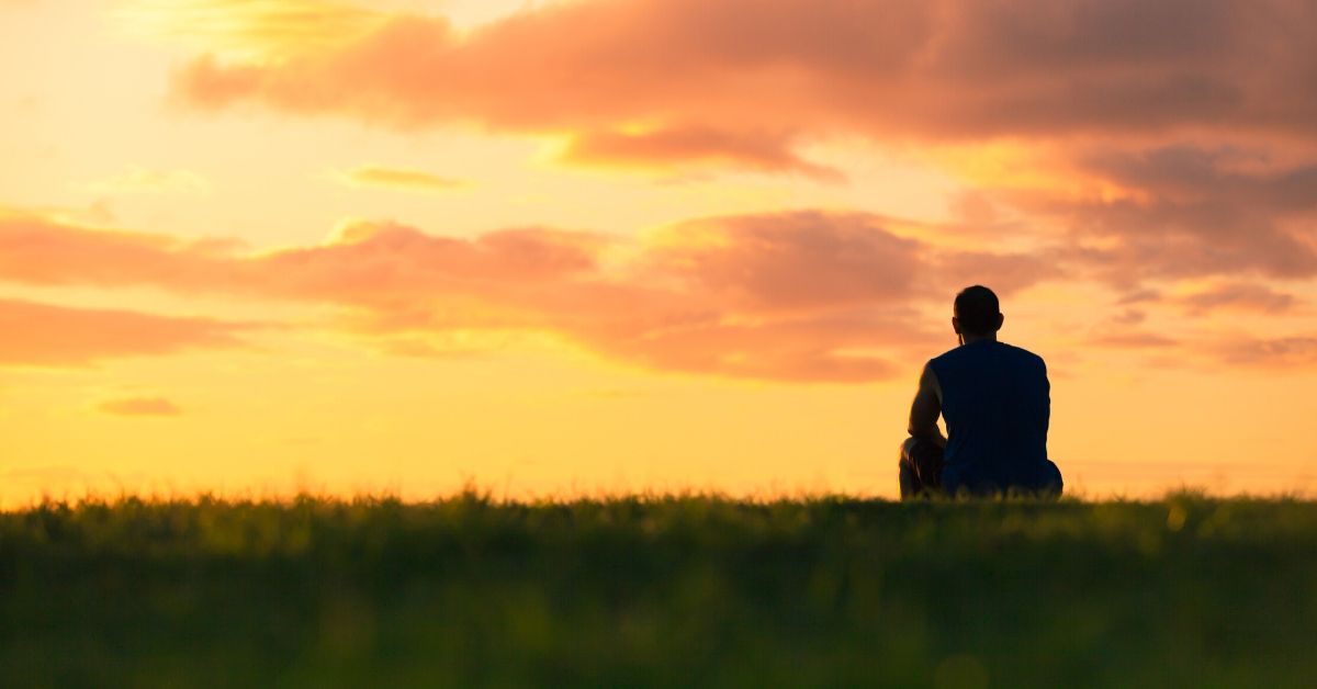 photo of a silhouette of a man sitting on a hill at sunset