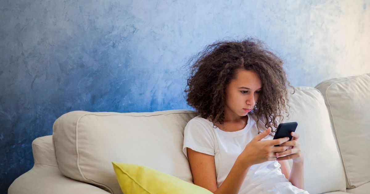 photo of a young girl sitting on a couch looking at her phone