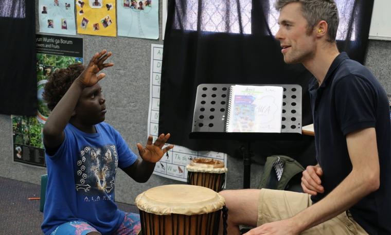 a teacher and indigenous student playing a hand drum