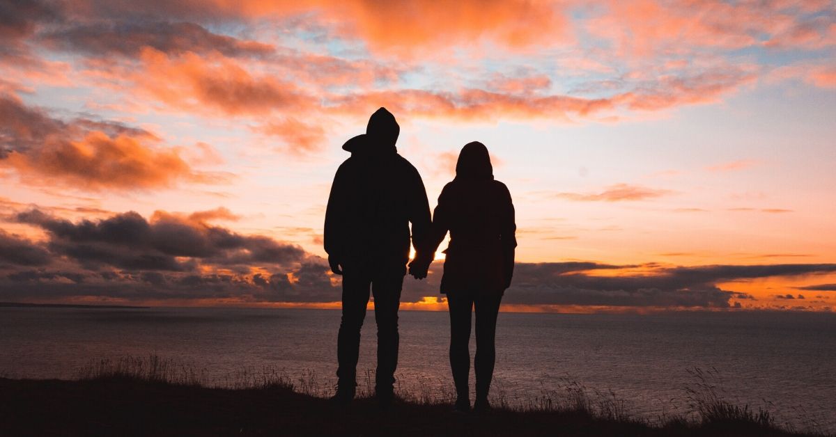 photo of a silhouette of a couple holding hands at dusk looking over the ocean