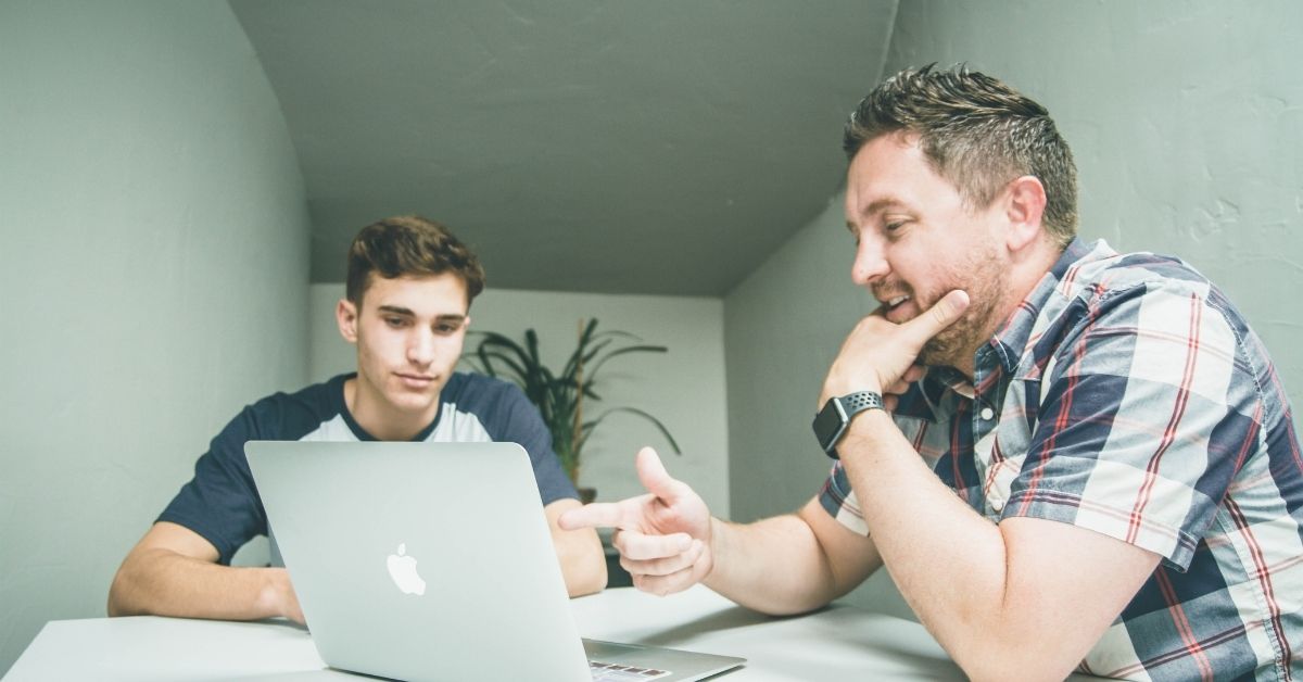 two men talking and gesturing to laptop