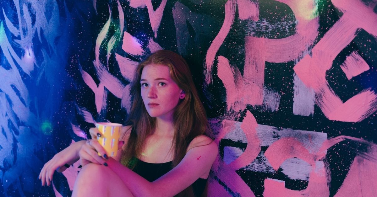 teen leaning against a wall with a cup in hand