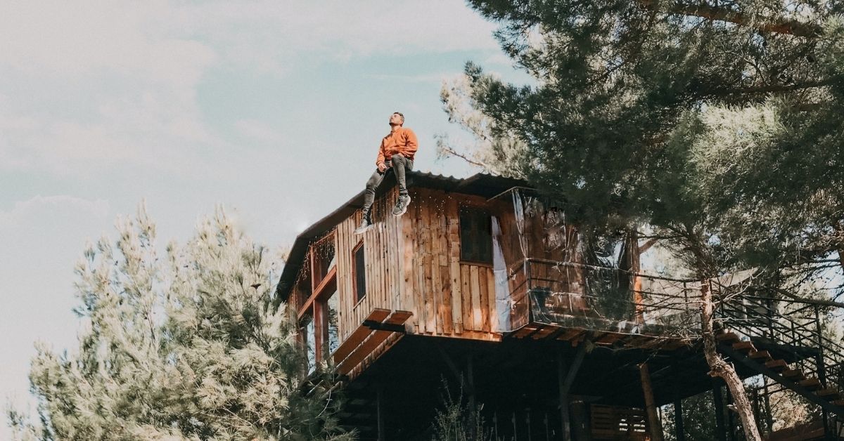 man sitting on top of a treehouse gazing upwards