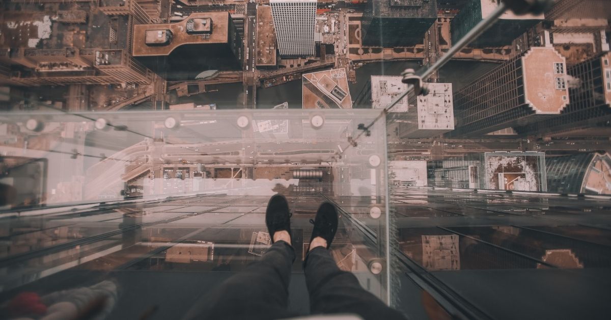 a person standing on the edge of a building sky deck with a glass floor overlooking a city