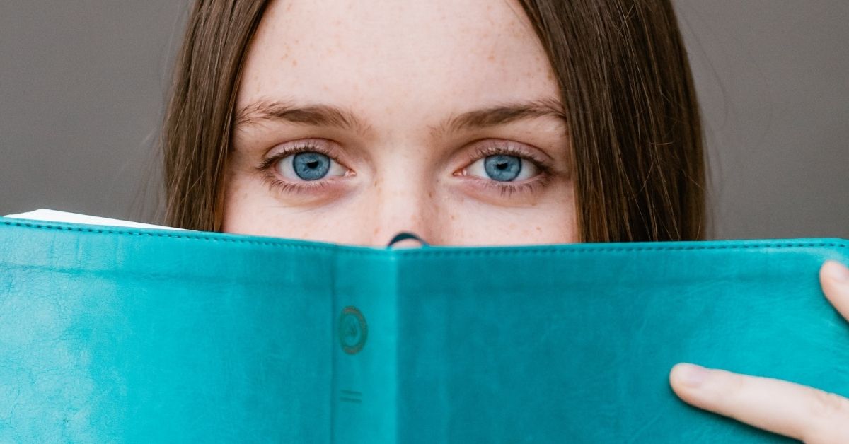 a girl's eyes peek up behind a blue book in front of her face