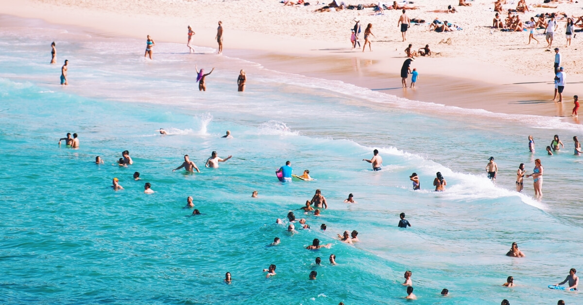 crowds swimming ocean and on sunbathing on beach