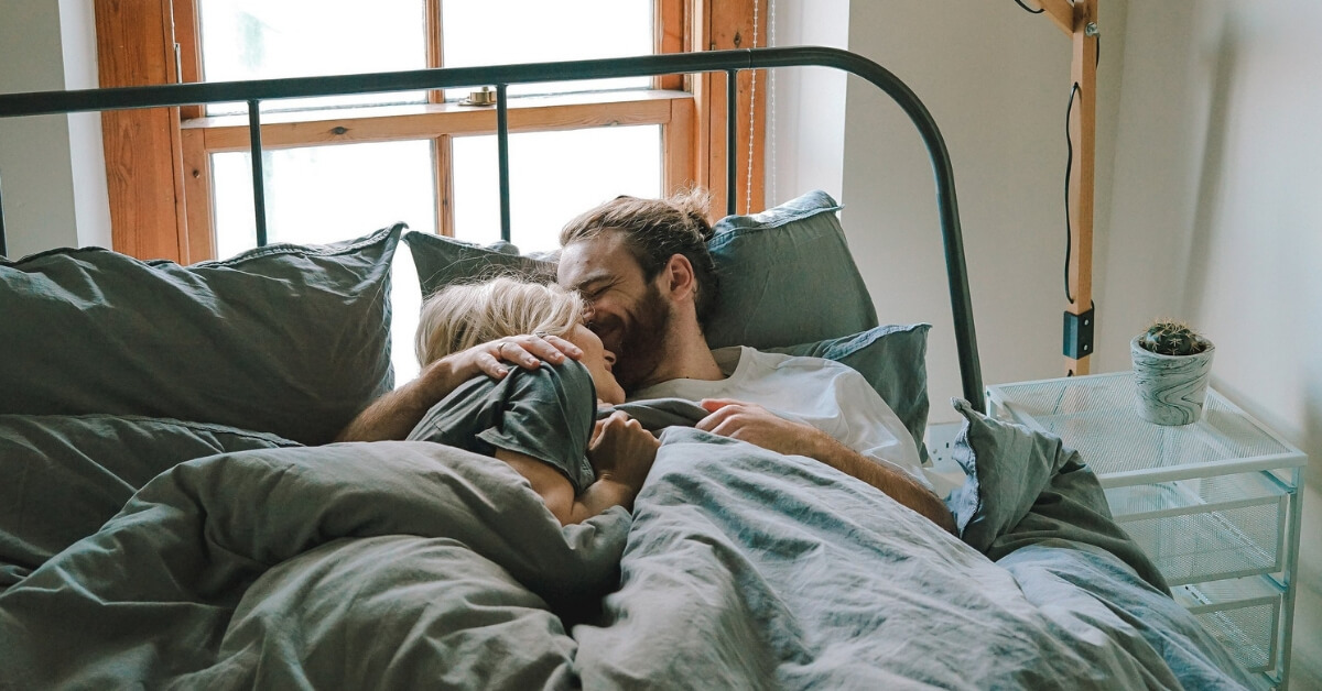 couple snuggling in bed with man kissing woman on the forehead