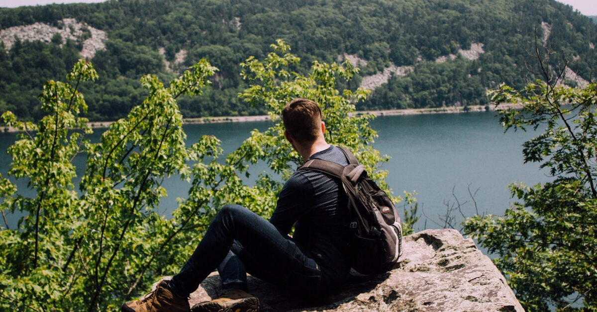man sitting on a high rock overlooking a body of water
