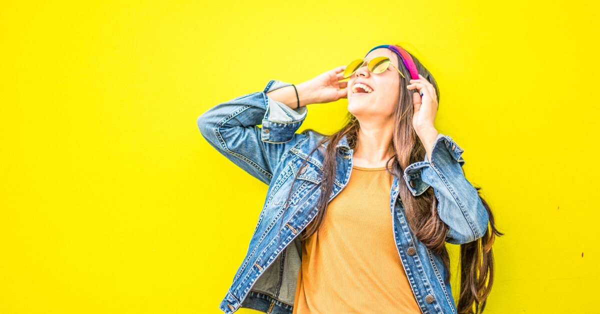 happy woman wearing sunglasses in front of a yellow wall