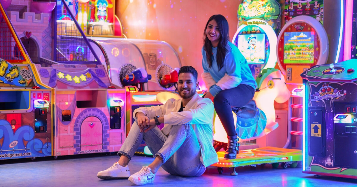 man and woman sitting in a colourfully lit arcade