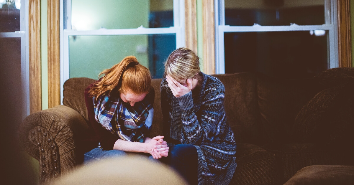 two women sitting on a couch grieving