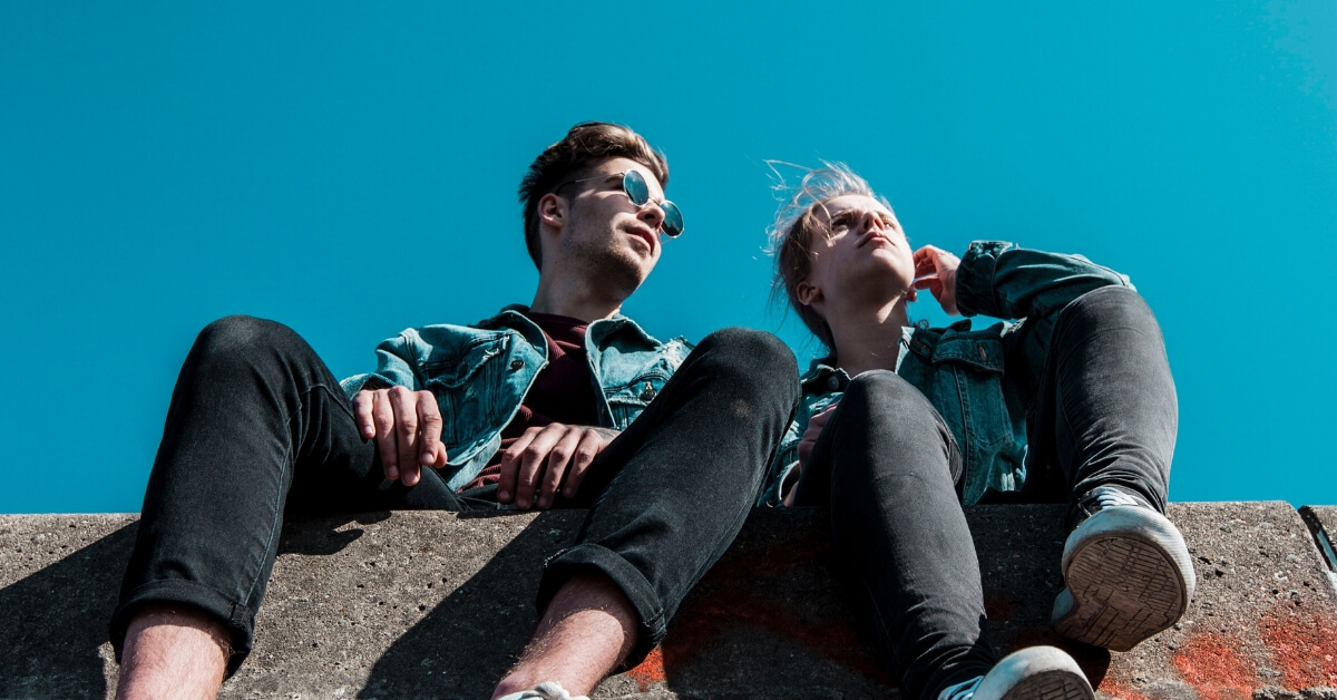 low angle looking up at two young people sitting on a brick wall