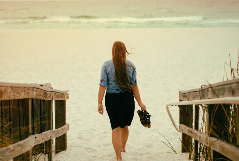 Woman walking toward the ocean barefoot