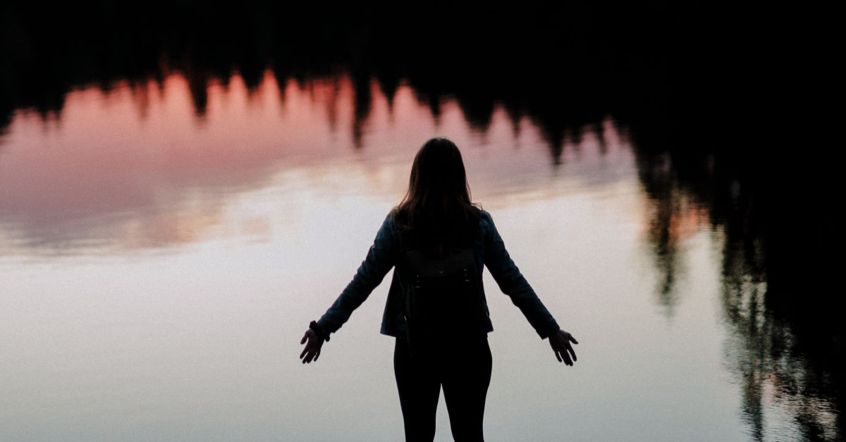 woman standing by lake at sunset