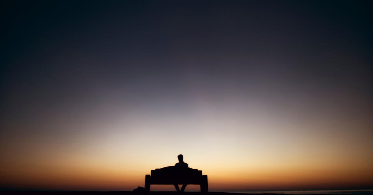 man sitting on park bench against sunset