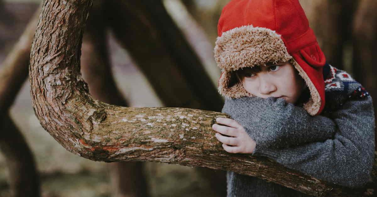 boy hugging tree branch with bored look