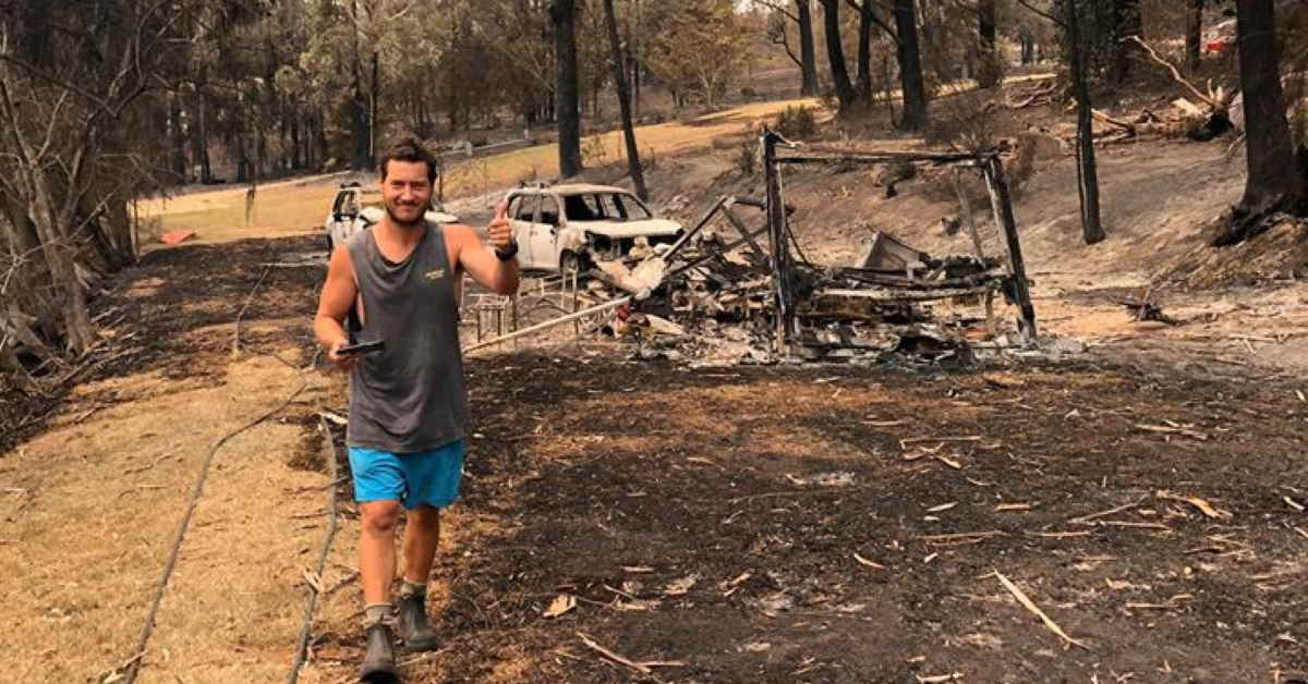 Andrew Flaxman walking in burned bushland with his burnt out car and caravan behind him
