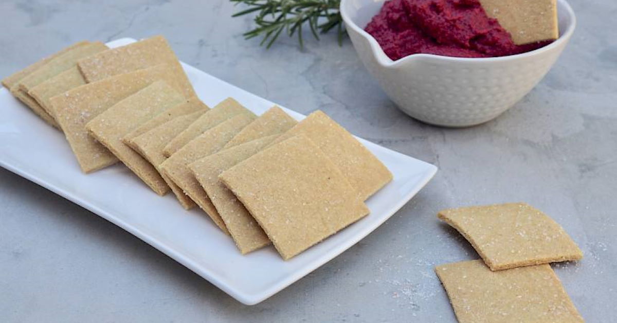 crackers on a plate with a bowl of beetrot dip in the background