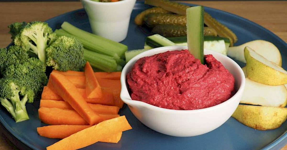 a bowl of bright pink beetroot dip surrounded by vegetables for dipping