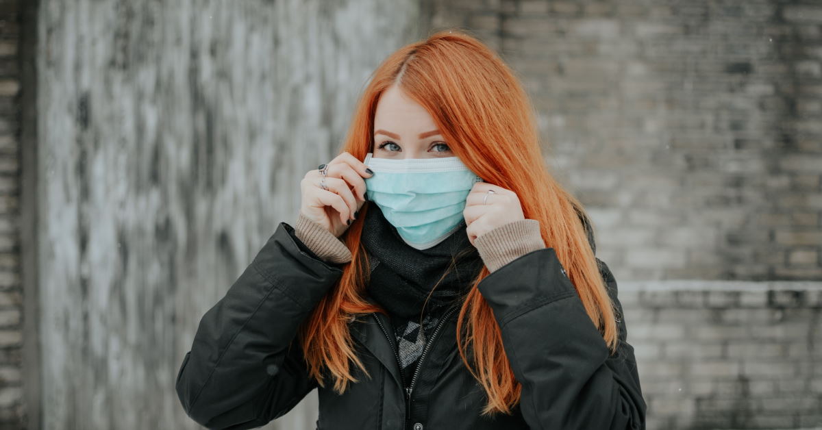 Woman with red hair putting on medical face mask