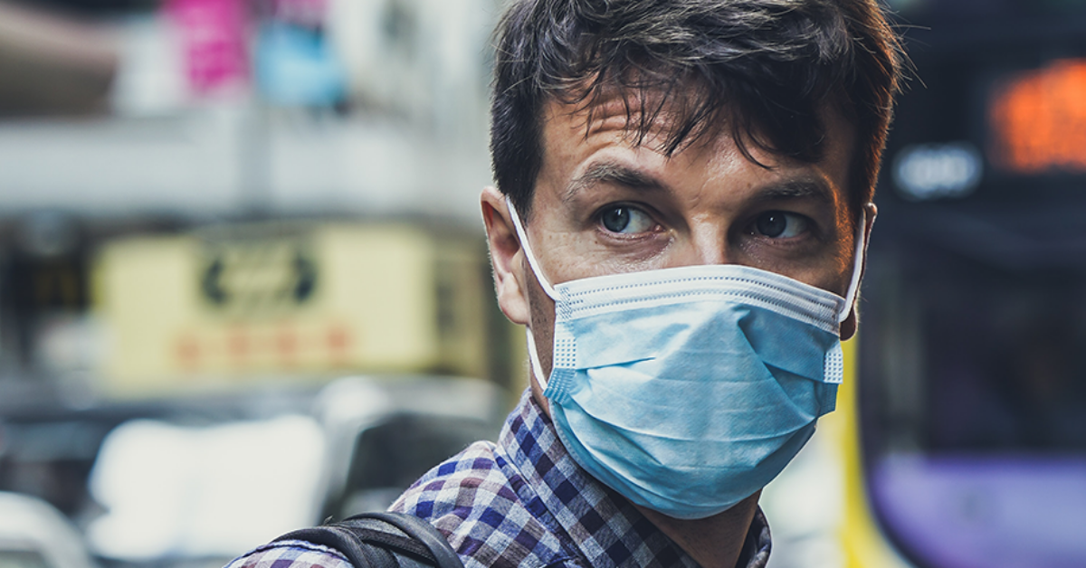 close up of man in a flu mask with blurred out street behind him