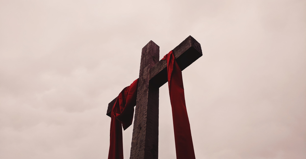 looking up at wooden cross towards sky red sash draped over cross