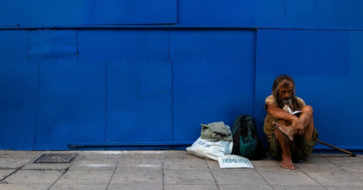 dishevelled homeless man sitting against a blue wall