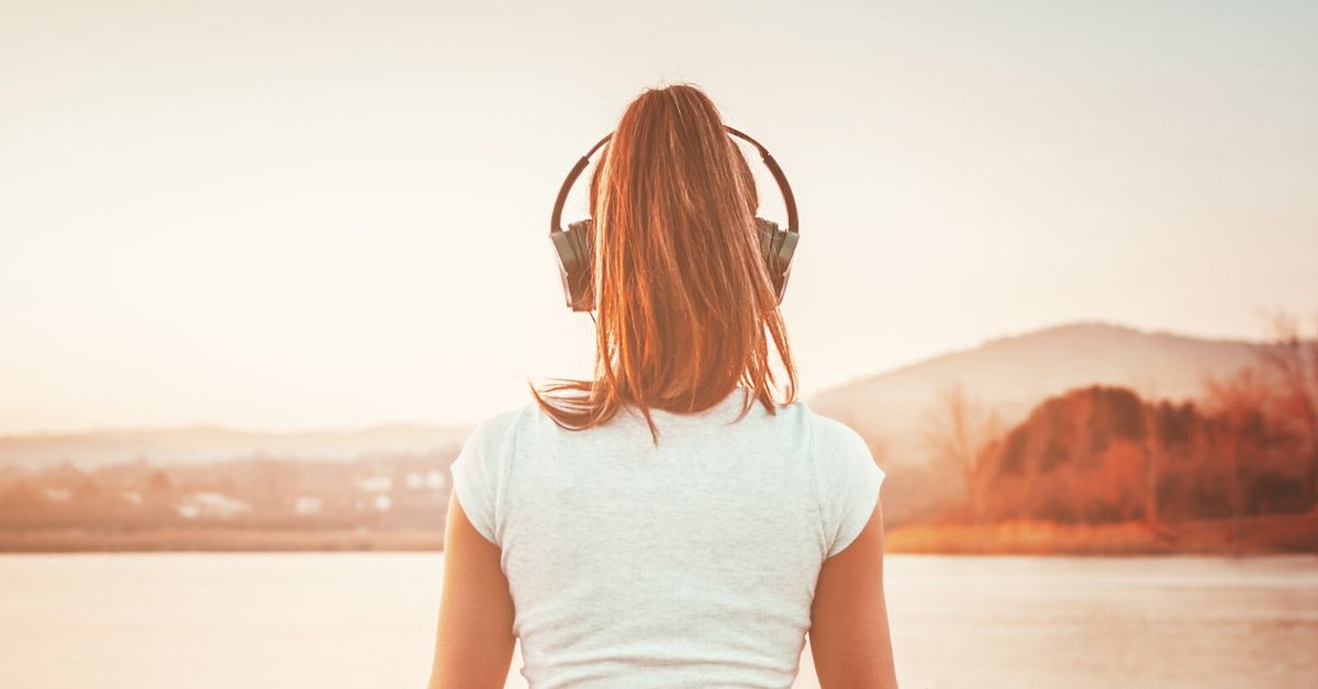 photo of the back of a woman wearing headphones looking out over a lake