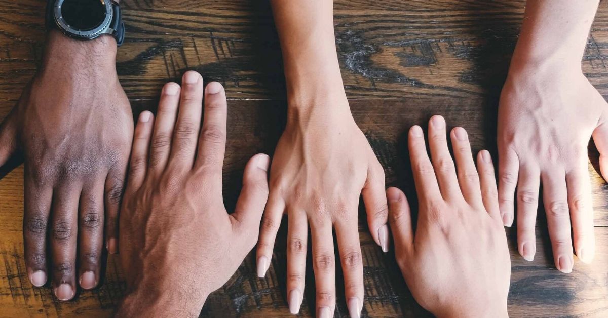 photo representing the concept of migration which depicts different coloured skin toned hands side by side on a wooden table
