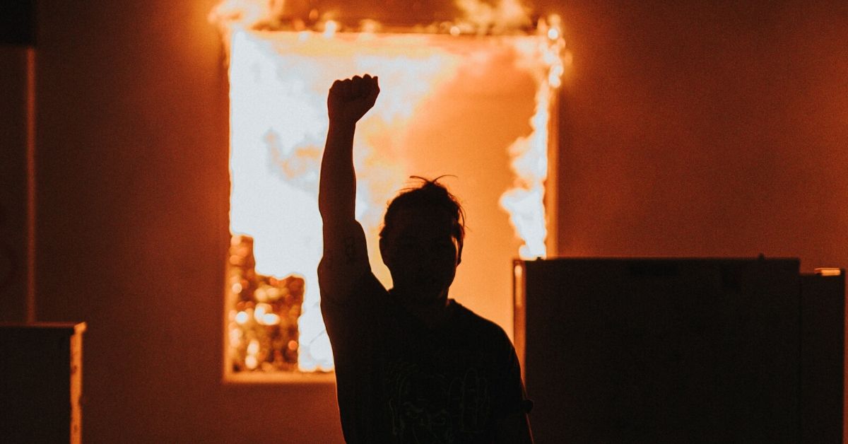 photo depicts a silhouette of a person with their fist raised in front of a fire