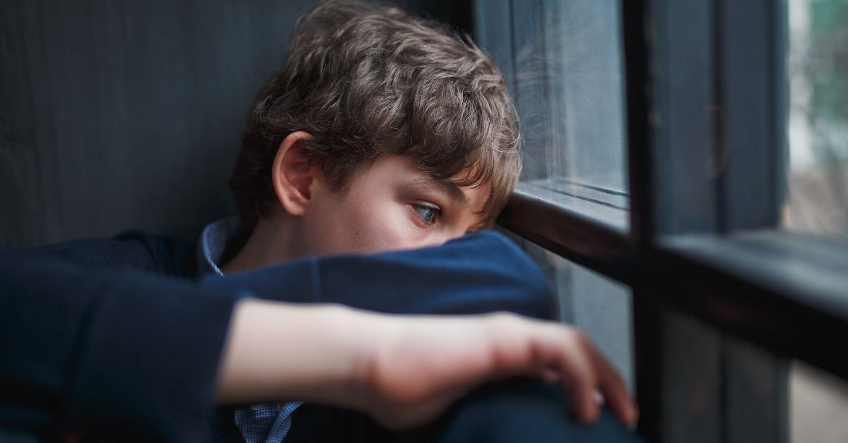 boy sitting gazing out the window with arms around knees