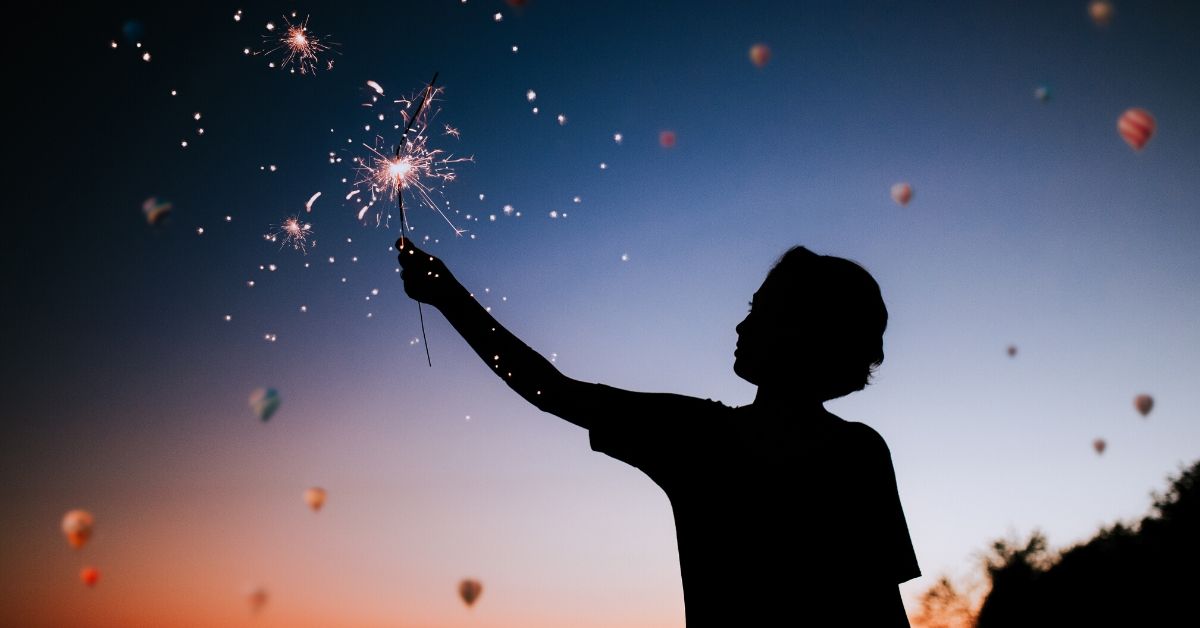 photo depicts a silhouette of a boy at sunset holding a sparkler to the sky