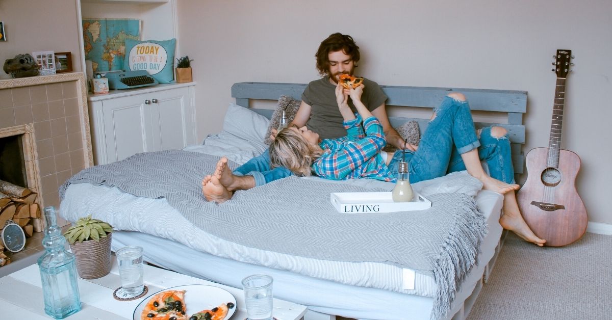 girl feeds her boyfriend pizza on a bed