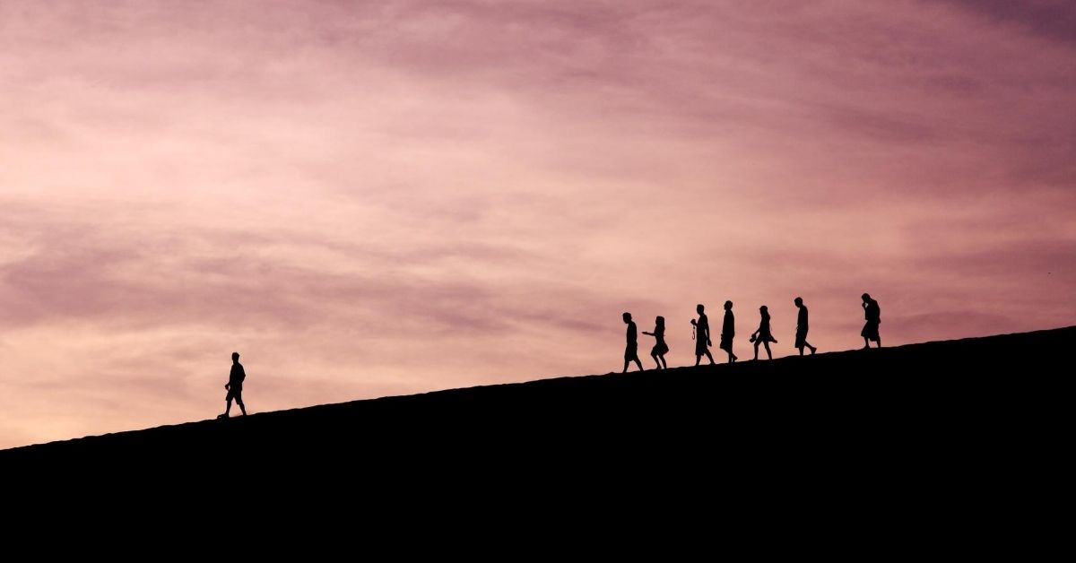 silhouette of a leader walking in front of a group down a mountain