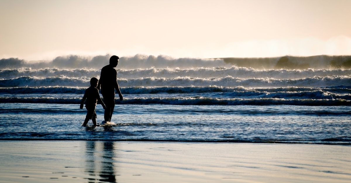 a boy walks with his dad on the beach