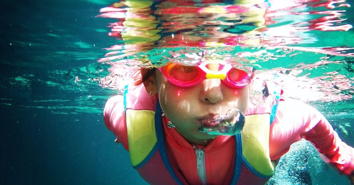 underwater shot of kid swimming wearing goggles and swimming cap