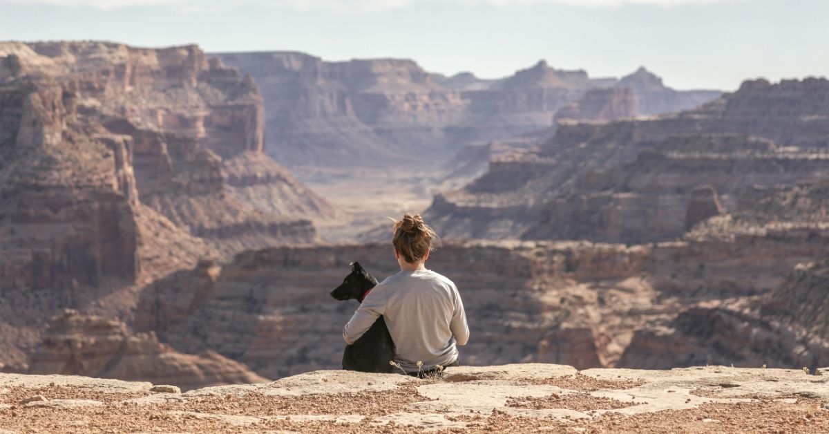 woman and her dog sitting looking out over mountain range