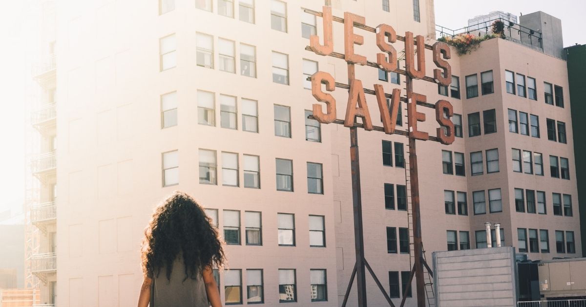 woman sitting on a wall overlooking a large sign which says jesus saves