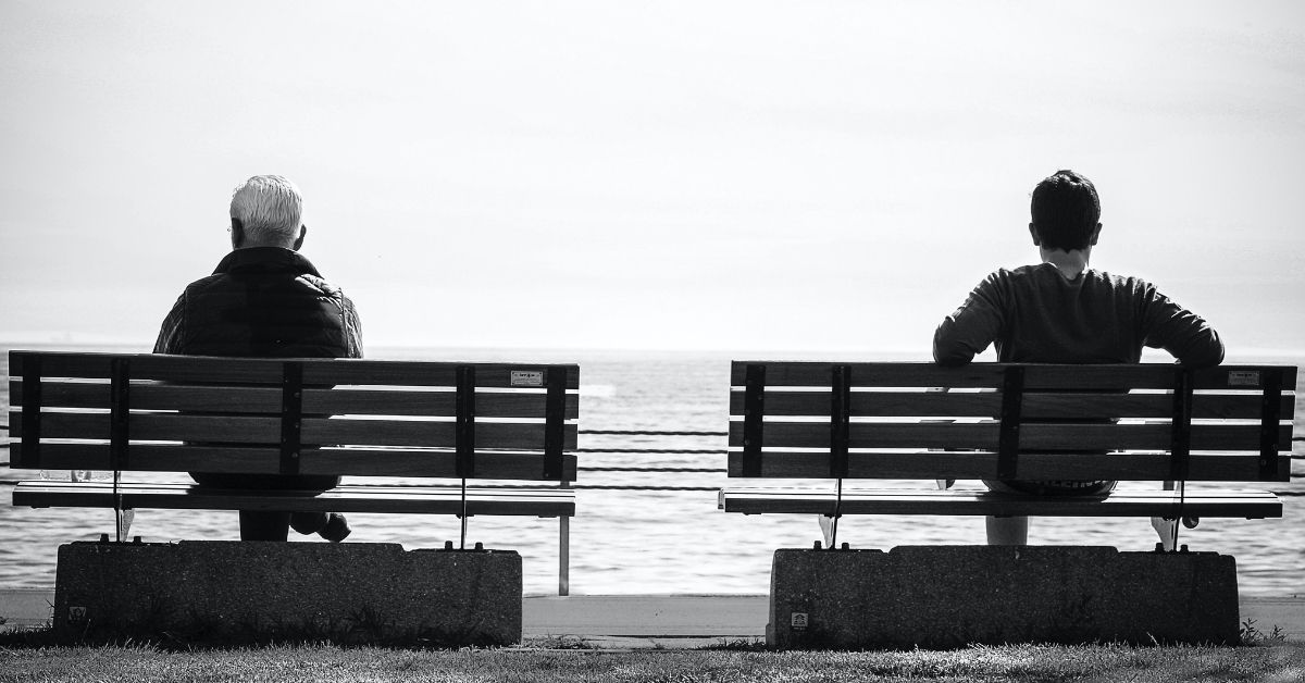 two men sitting on separate park benches gazing forward