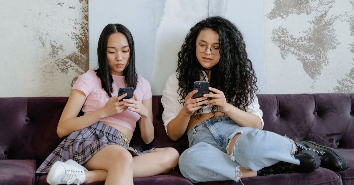 two girls in their late teens / early 20s on their phones