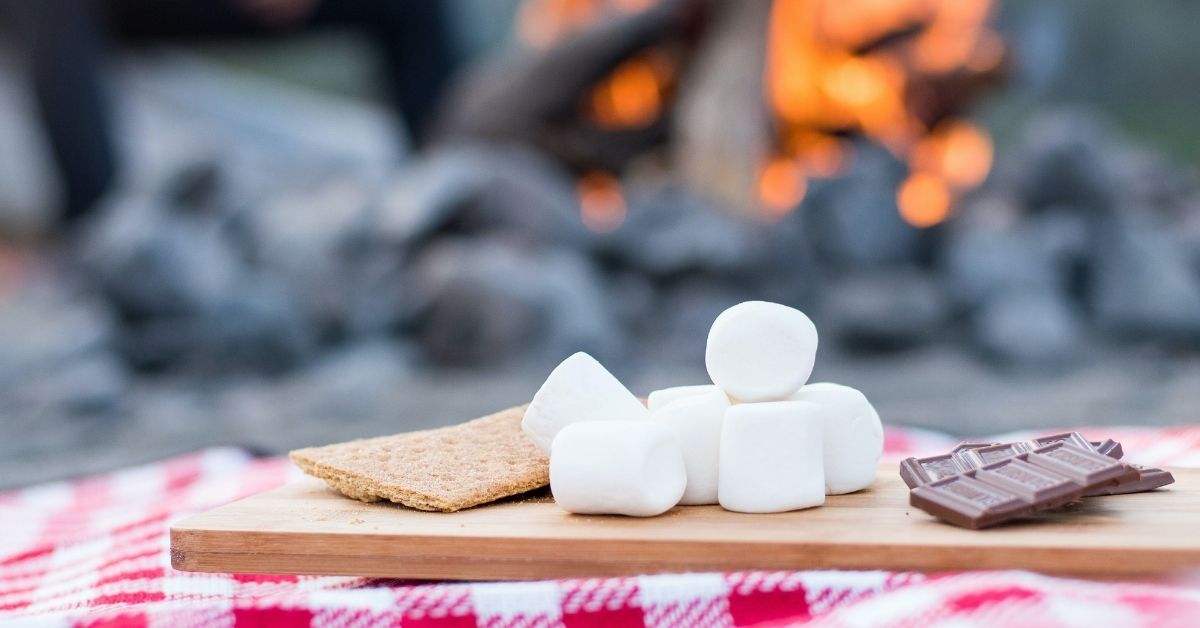 ingredients for smores in front of a campfire - biscuits, marshmallows and chocolate